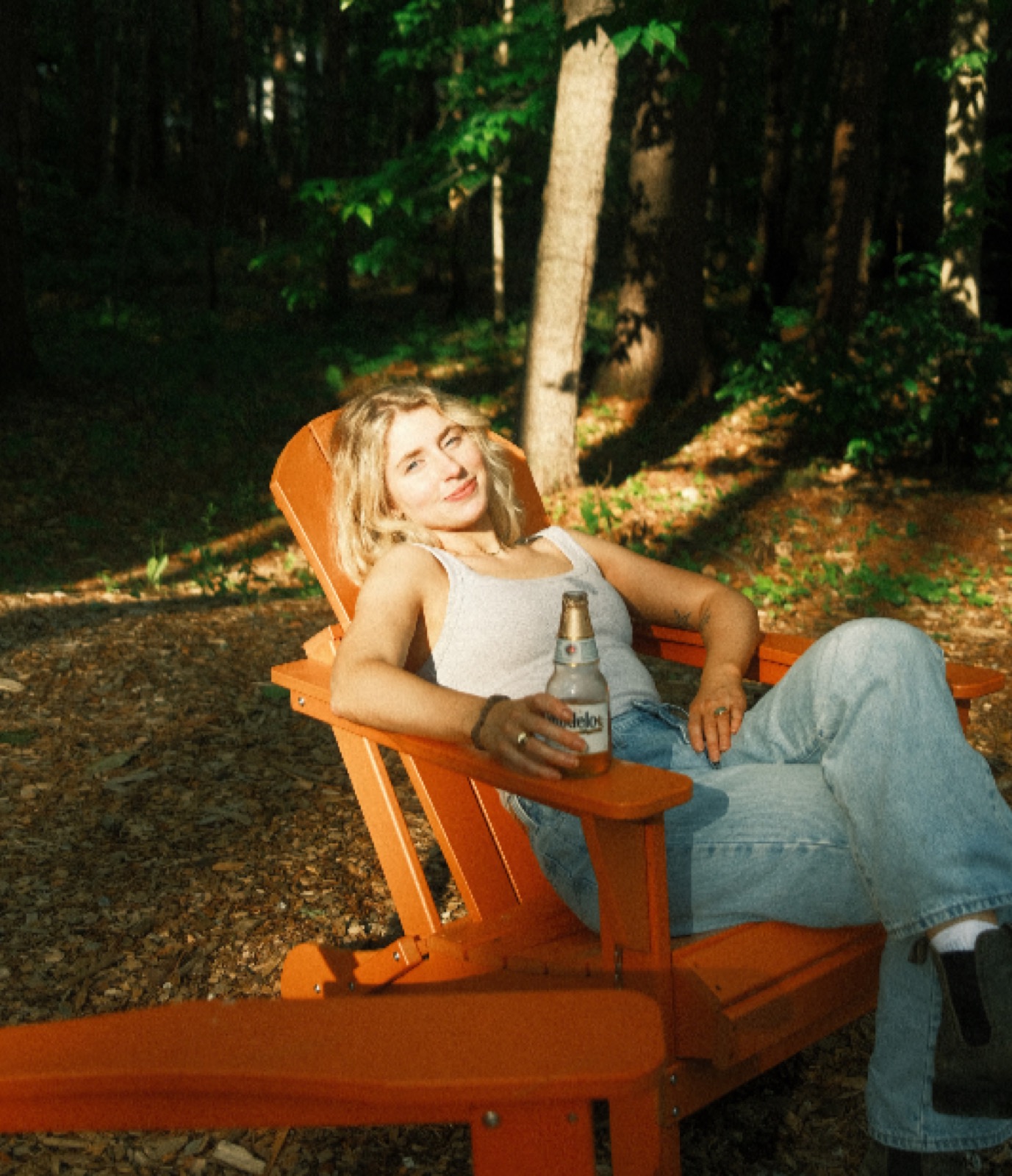 Orange Adirondack chairs around a fire pit in the woods