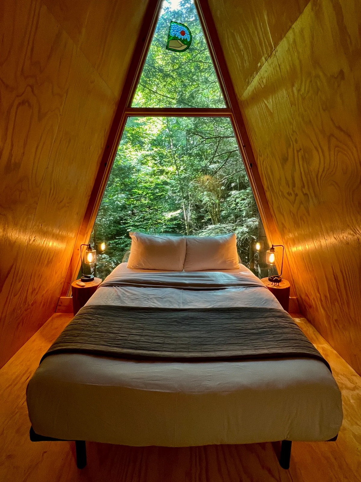 The queen bed under the big window inside a Cozy A-frame