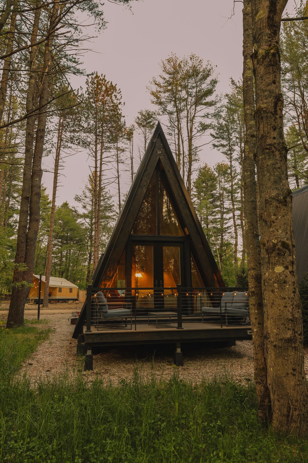 An Escape A-frame cabin glowing at dusk in the woods